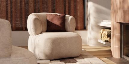 Lichte, ronde fauteuil met bruin kussen op een tapijt naast een haard, met warme gordijnen en zacht invallend licht.