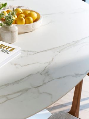 Close-up van een lichte eettafel met subtiel marmerpatroon en afgeronde rand, gedecoreerd met een schaal citroenen, een vaasje en een boek.
