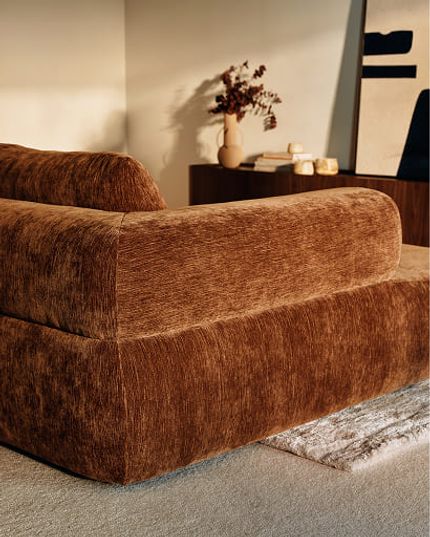 Canapé brun aux formes arrondies dans un intérieur chaleureux avec meuble foncé et touches décoratives.