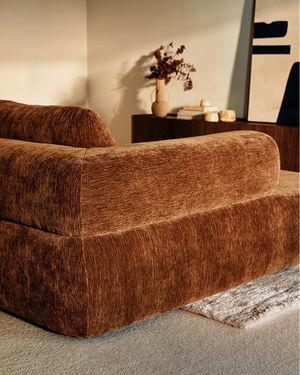 Canapé brun aux formes arrondies dans un intérieur chaleureux avec meuble foncé et touches décoratives.