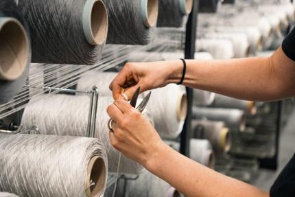 Medewerker knipt garen tussen spoelen in een textielproductieomgeving.