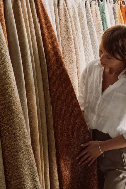 Femme examinant des tissus dans un showroom, entourée d'une série d'échantillons de textiles dans différentes teintes terreuses.