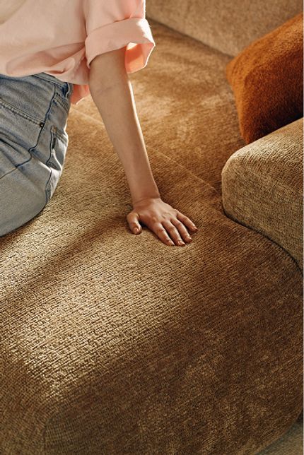 Gros plan du canapé Sarpi en tissu chaud et mélangé ; une personne repose sa main sur l'assise douce.
