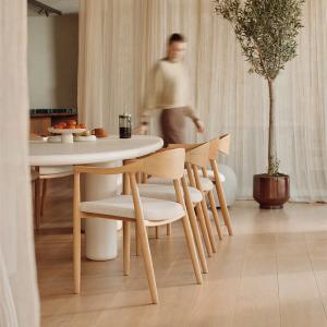 Table Artisano dans une salle à manger lumineuse avec chaises en bois et assises tissu; fruits et café sur la table.