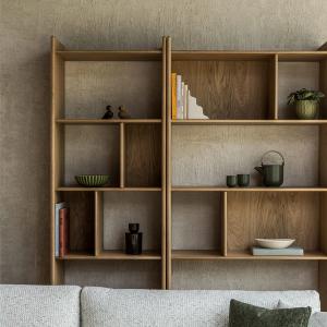 Une étagère en bois avec des compartiments ouverts, remplis de livres et d'objets décoratifs. À l'avant, un canapé confortable avec des coussins, créant une ambiance chaleureuse et accueillante.