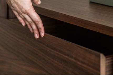 Close-up van een hand die een houten lade van een dressoir opentrekt, met zichtbare houtnerf en strakke afwerking.