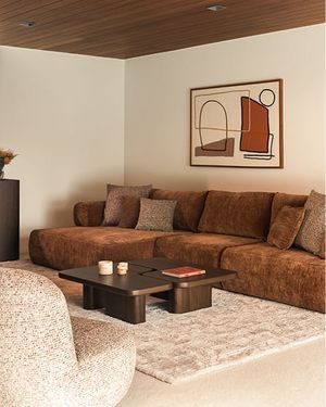 Salon chaleureux avec canapé d’angle brun, table basse foncée et fauteuil dans des tons neutres.
