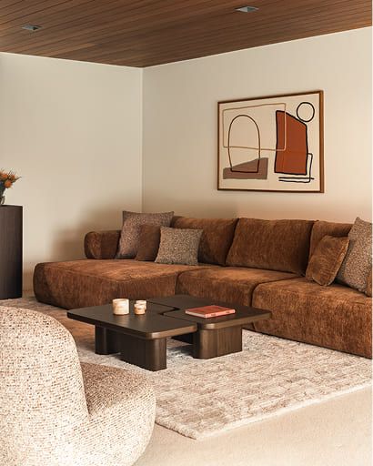 Warme woonkamer met een bruine hoekzetel, donkere salontafel en fauteuil in neutrale tinten.