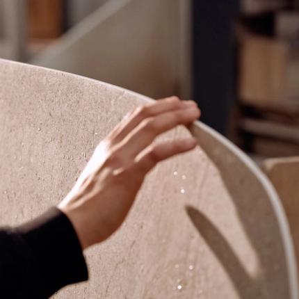 een close-up van een vakman die de rand van een Curvo tafel aanraakt, waarbij de gladde afwerking en het subtiele ontwerp van het tafelblad goed zichtbaar zijn.