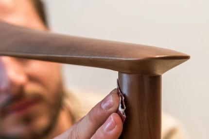 Persoon schuurt de houten armleuning van een stoel; close-up van hand en afgeronde hoek in warme houttint.