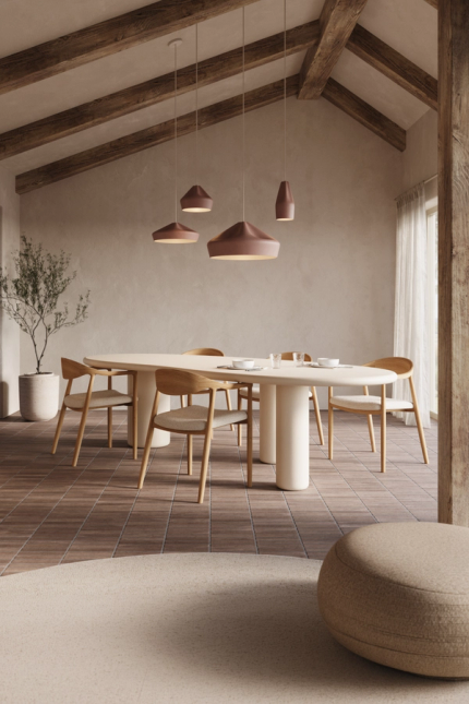 Ovale eettafel met houten stoelen in warme eetkamer met houten balken, hanglampen en groot raam.