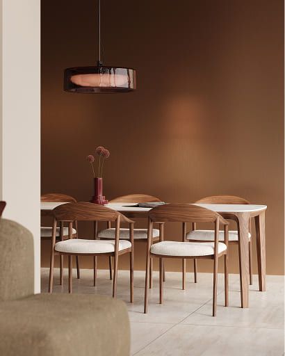 Eetkamer met houten stoelen met lichte zittingen rond een eettafel met licht blad, tegen een warme bruine wand.