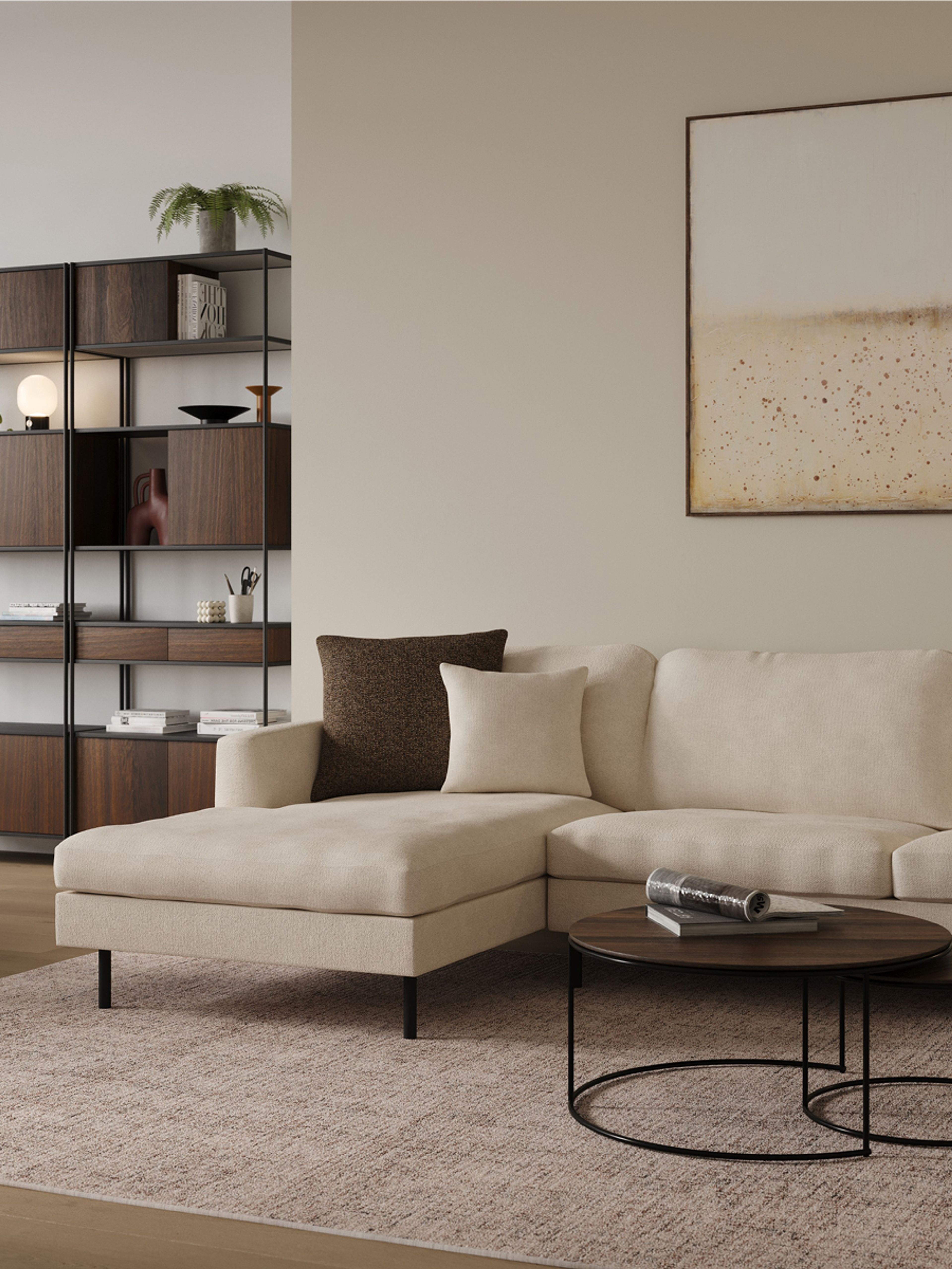 Detail van een beige hoekzetel met kussens, ronde zwarte salontafel en open kast met donkere houtvakken en planten.