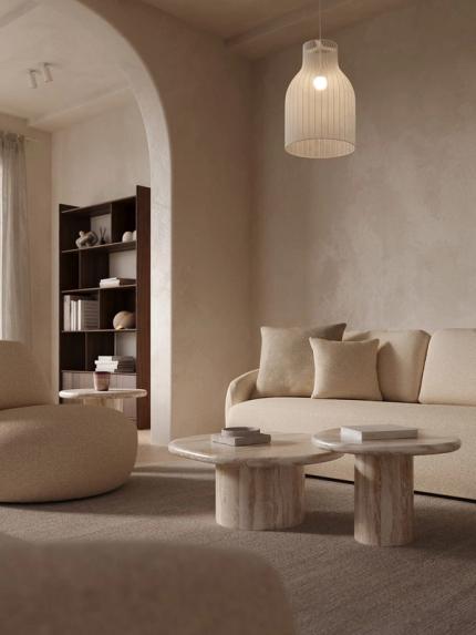 Zetel Tomar in zachte beige stof met ronde vormen, marmeren salontafels, hanglamp en hoge houten boekenkast in de nis.