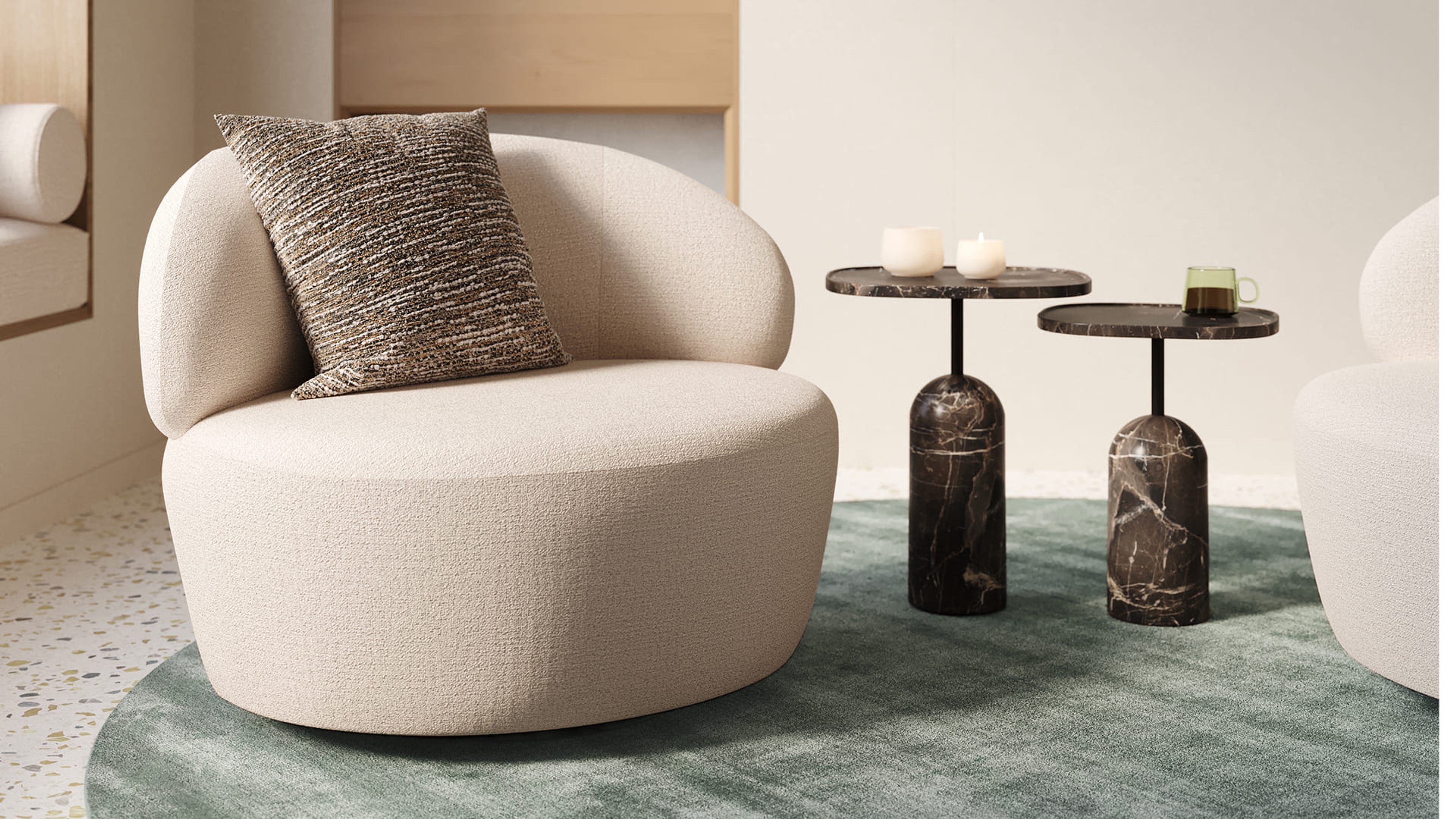 Norcia fauteuil met ronde, organische vorm in crèmekleurige stof, afgewerkt met een decoratief sierkussen in gemêleerde bruintinten.