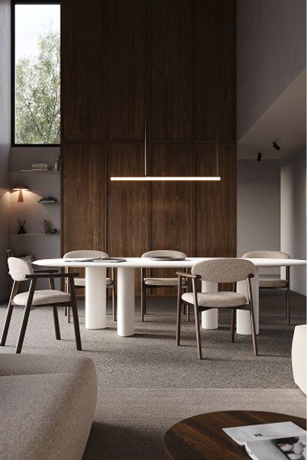 Salle à manger contemporaine avec longue table blanche, chaises rembourrées, suspension et grand placard en bois, éclairée par de larges fenêtres.
