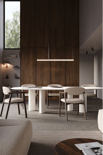 Salle à manger contemporaine avec longue table blanche, chaises rembourrées, suspension et grand placard en bois, éclairée par de larges fenêtres.