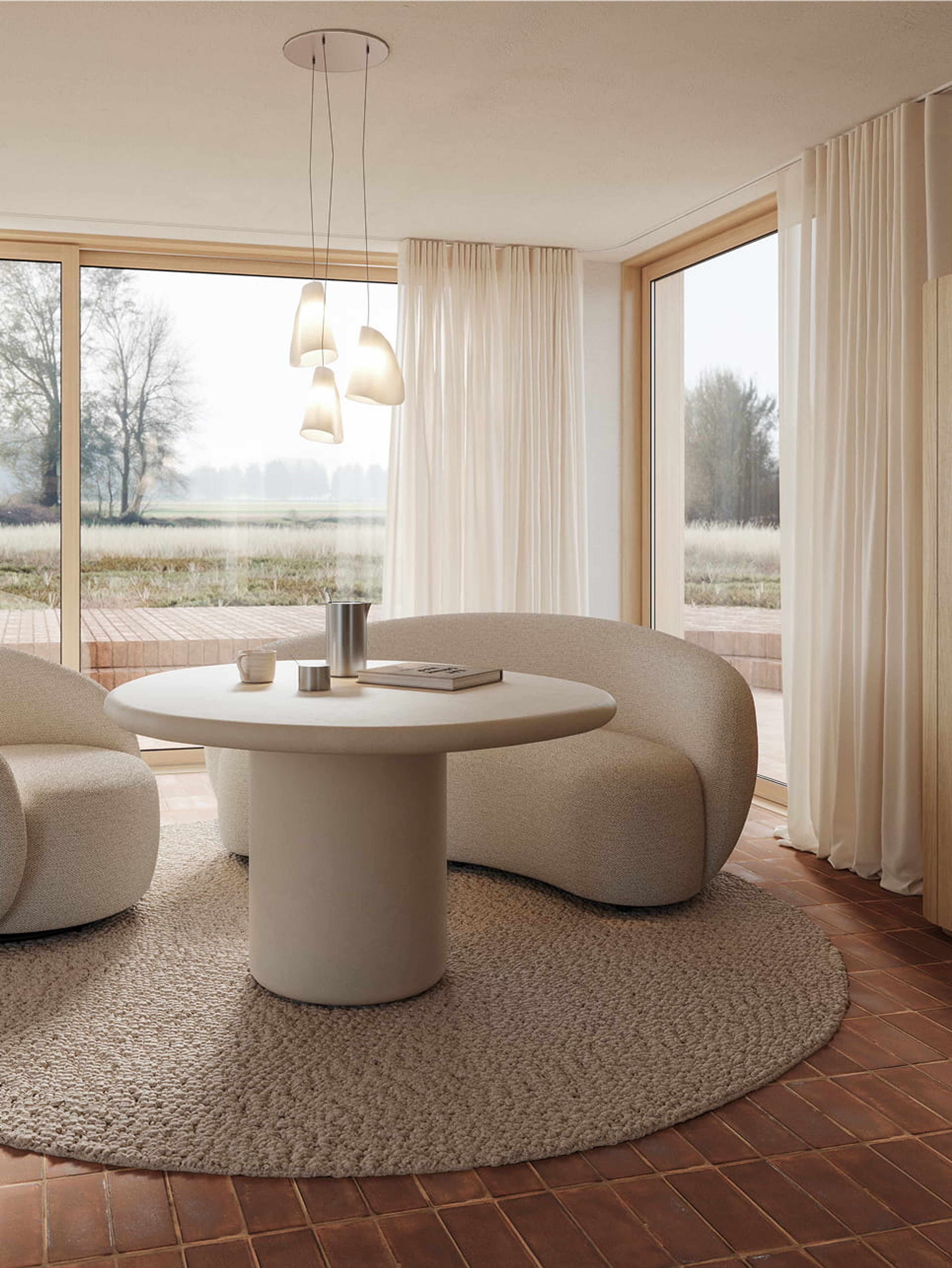 Ronde Artisano eettafel met centrale poot in een lichte ruimte, gecombineerd met twee afgeronde loungestoelen en grote ramen.
