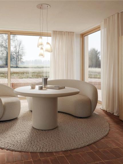 Ronde Artisano eettafel met centrale poot in een lichte ruimte, gecombineerd met twee afgeronde loungestoelen en grote ramen.