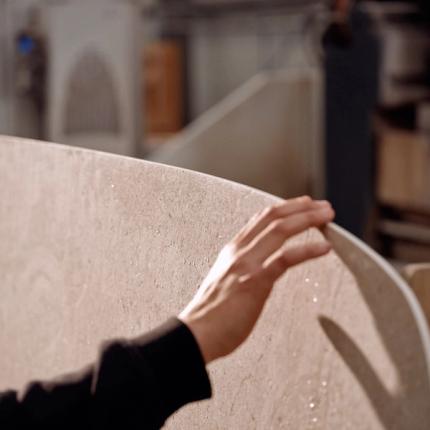 Une main touchant délicatement le bord d'un matériau poli, mettant en évidence le savoir-faire et l'attention aux détails dans le processus de fabrication.