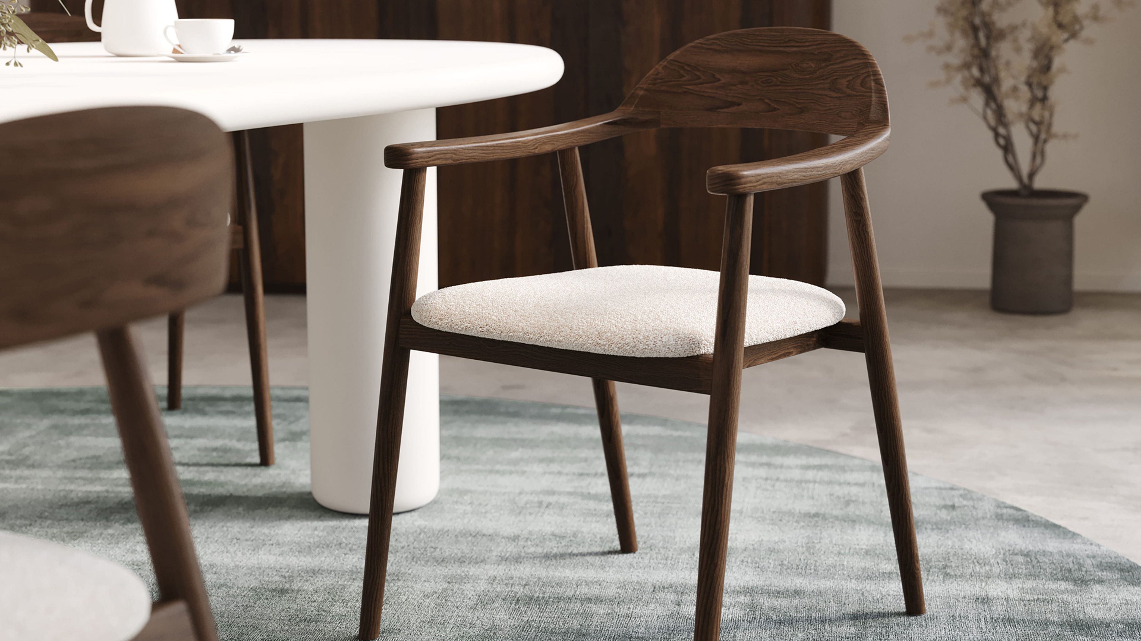 Comino stoel in donker hout met lichtbeige zitting bij witte ronde eettafel op groenblauw vloerkleed.