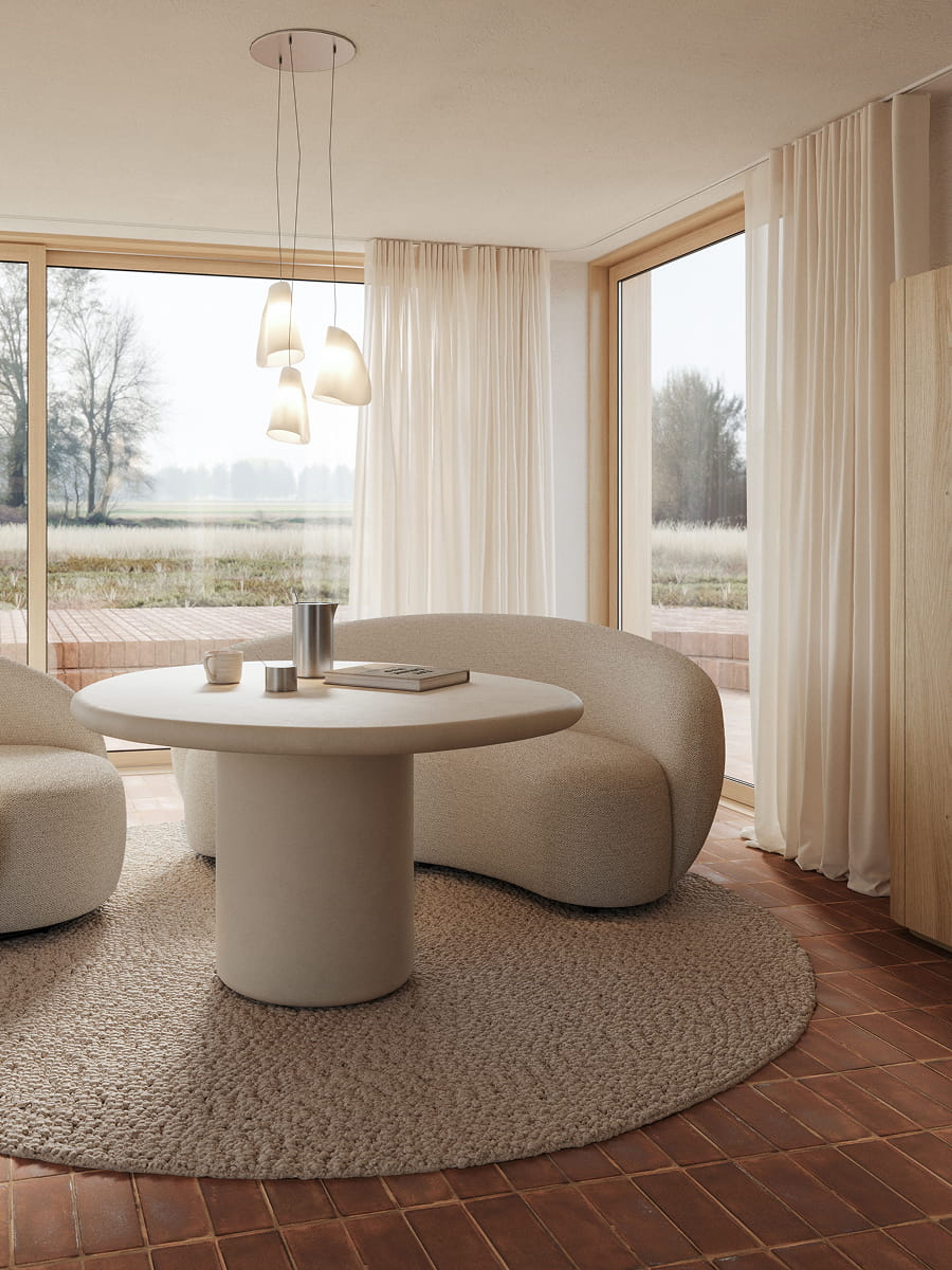Table à manger ronde Artisano avec pied central dans un intérieur lumineux, associée à deux fauteuils arrondis et de grandes fenêtres.