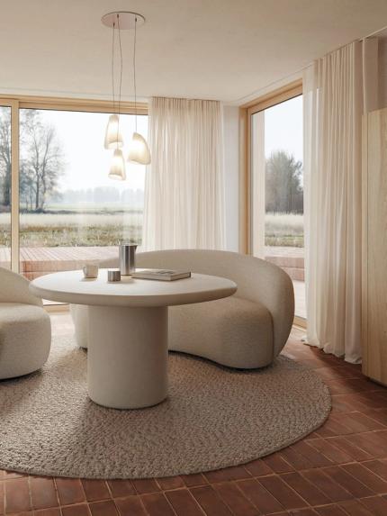 Table à manger ronde Artisano avec pied central dans un intérieur lumineux, associée à deux fauteuils arrondis et de grandes fenêtres.