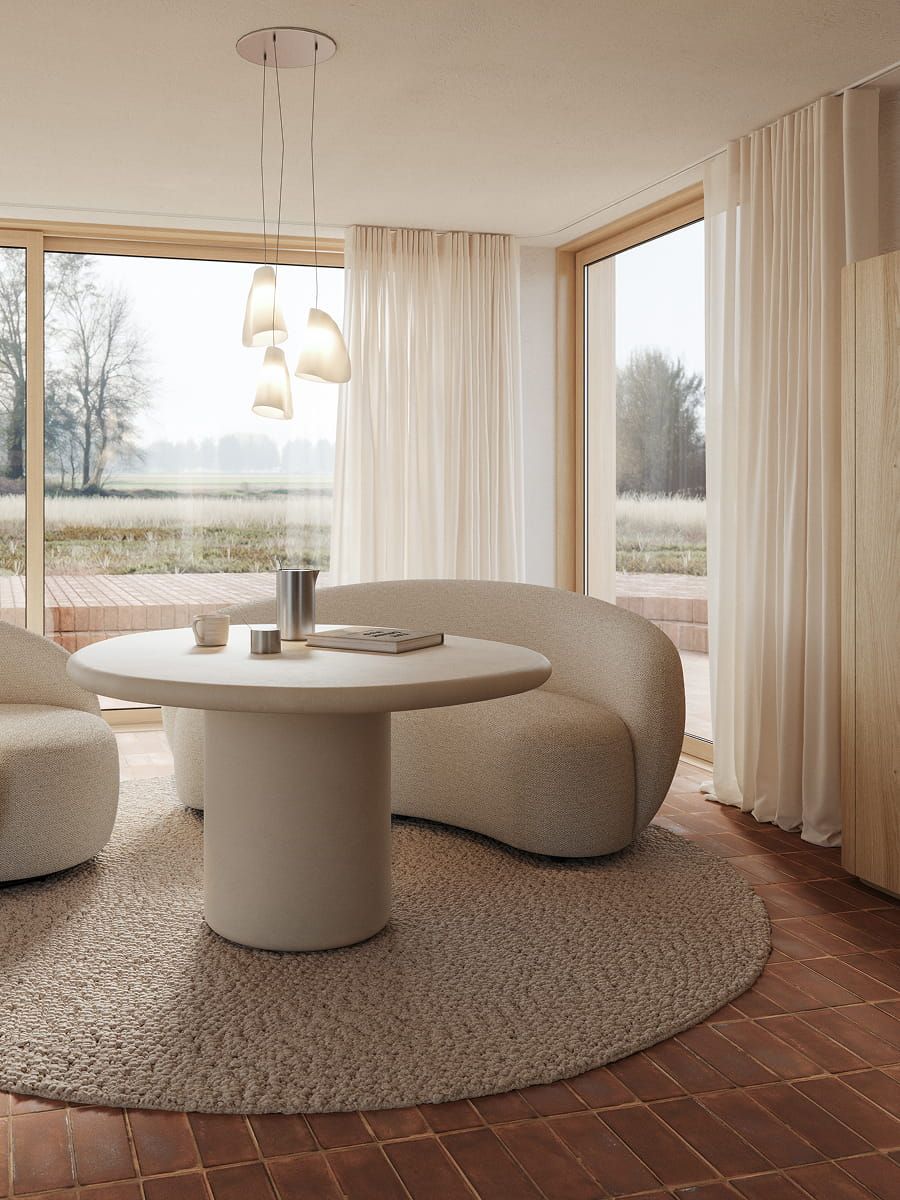 Table à manger ronde Artisano avec pied central dans un intérieur lumineux, associée à deux fauteuils arrondis et de grandes fenêtres.