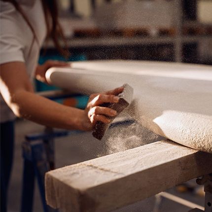 Hand die een Claylime-tafel schuurt, met fijne stofdeeltjes in het licht, in een atelier.