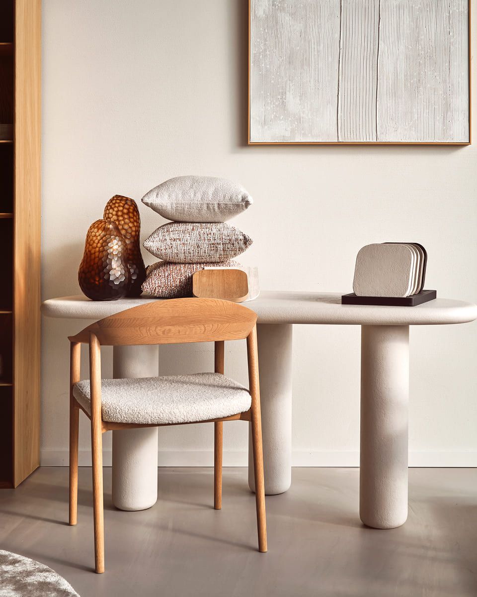 Eettafel met houten stoel, gestapelde kussens en decoratieve objecten.