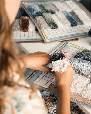 Persoon vergelijkt stalen van tapijtgarens in verschillende kleuren en texturen.