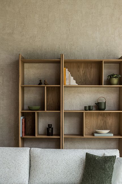 Houten boekenkast met open vakken en afgeronde staanders, gestyled met boeken en keramiek tegen een ruwe muur.