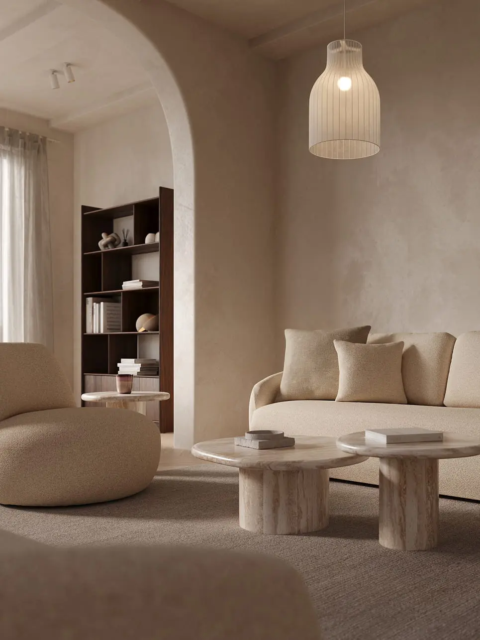 Fauteuil Gatto en tissu bouclé clair dans un salon chaleureux, à côté d’un canapé beige et de deux tables basses rondes en marbre sur un grand tapis.