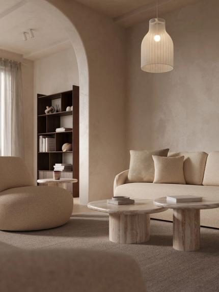 Fauteuil Gatto en tissu bouclé clair dans un salon chaleureux, à côté d’un canapé beige et de deux tables basses rondes en marbre sur un grand tapis.