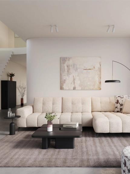 Canapé d’angle Campo beige avec assise profonde dans un salon moderne avec table basse noire, lampadaire et tons neutres.