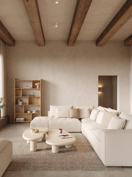 Beige hoeksofa in een rustige woonkamer met houten balken, open kast en organische salontafels op een neutraal tapijt.