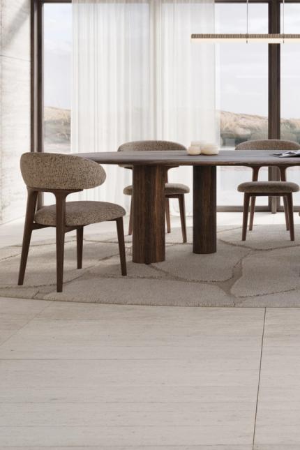 Donkerhouten eettafel met gestoffeerde stoelen en dressoir in een lichte eetkamer met grote ramen.