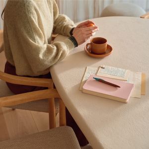 Personne assise à la table Artisano beige clair avec tasse et carnet, détail du plateau et de son bord.