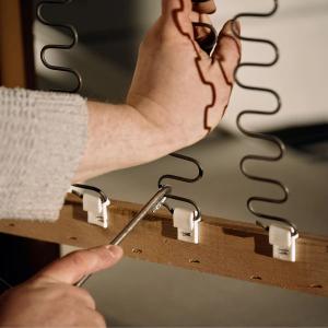 Gros plan sur des mains qui fixent des ressorts zigzag sur la structure en bois du canapé Sarpi pendant l’assemblage.