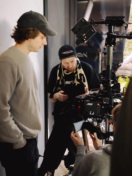 Regisseur en cameraman bekijken samen de camerabeelden op set, omringd door filmapparatuur tijdens de opnames.