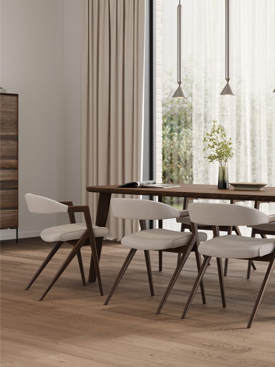 Donkere houten eettafel met licht gestoffeerde stoelen bij een groot raam met beige gordijnen, op een houten vloer.