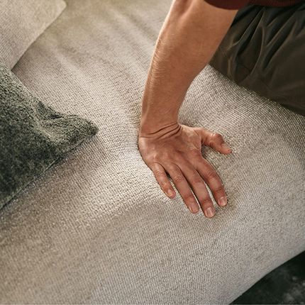 Hand drukt in de zachte, lichtbeige bekleding van de Tortona-zetel, close-up van de stoftextuur.