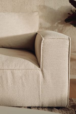 Gros plan d’un canapé beige au revêtement à la texture tissée, avec un large accoudoir et des coussins d’assise et de dossier moelleux.