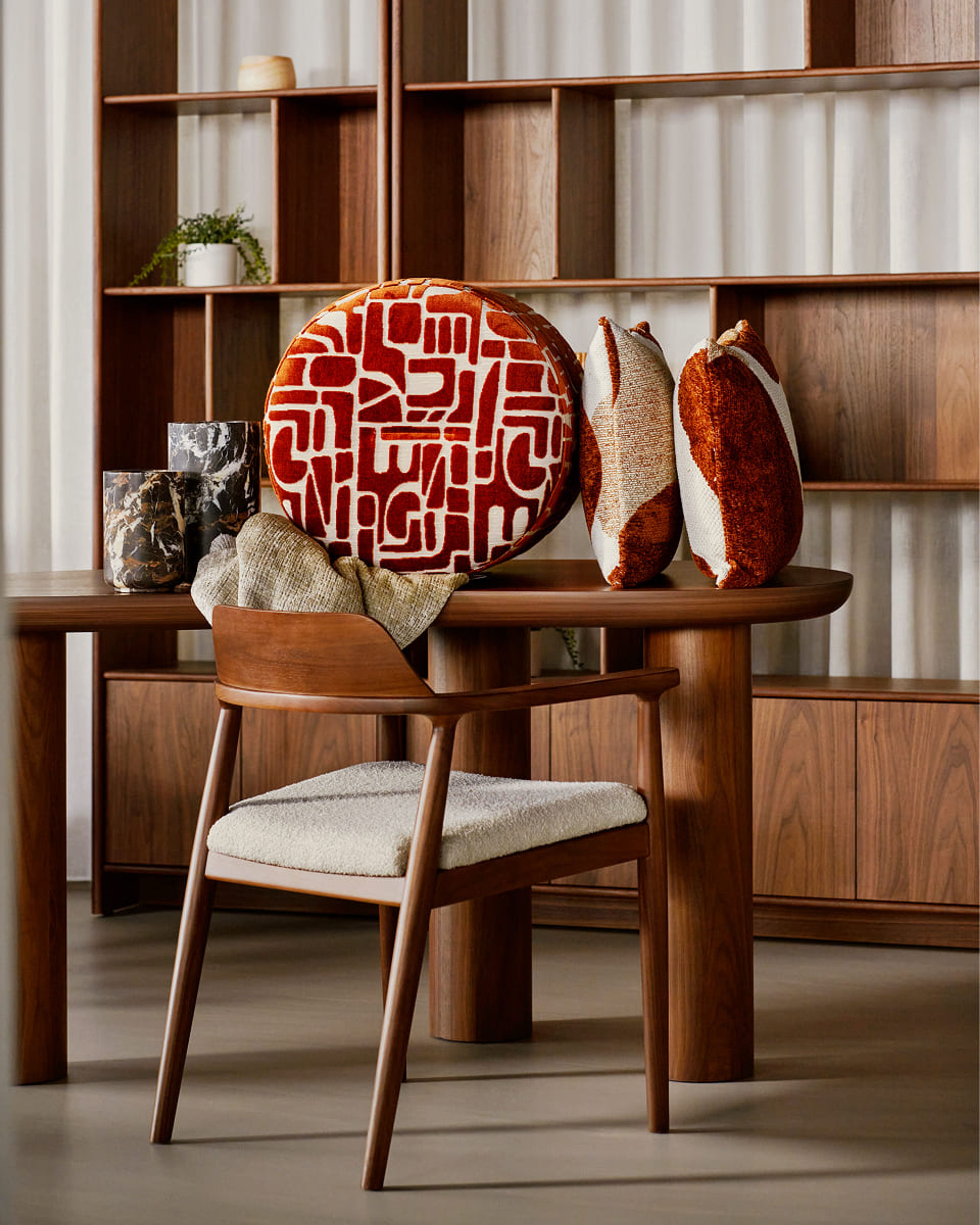 Houten tafel met decoratieve kussens, marmeren accessoires en een boekenkast.