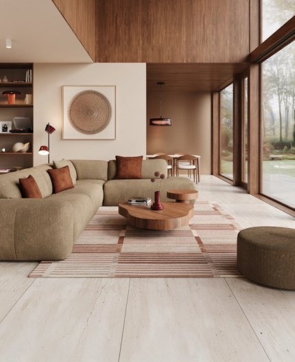 Salon beige avec canapé modulaire Sarpi, tables basses rondes en bois, tapis à rayures et grandes fenêtres donnant sur le jardin.