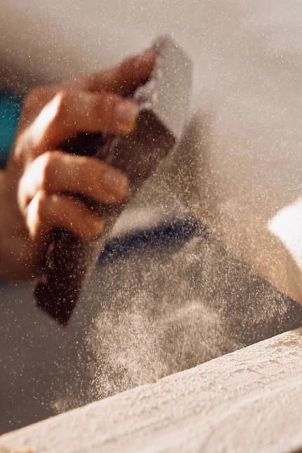 Hand schuurt een claylime tafelblad; fijn stof dwarrelt op in een atelier, close-up van vakwerk.