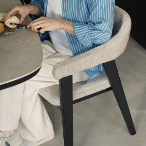 Detail van Gubbio stoel: lichtgrijze bekleding met armleuning en zwart houten onderstel, met iemand aan tafel.