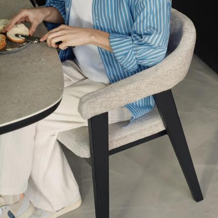 Detail van Gubbio stoel: lichtgrijze bekleding met armleuning en zwart houten onderstel, met iemand aan tafel.