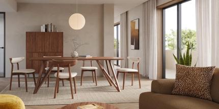 Salle à manger lumineuse avec longue table en bois et chaises rembourrées, suspension ronde, buffet en bois et grandes fenêtres avec rideaux.
