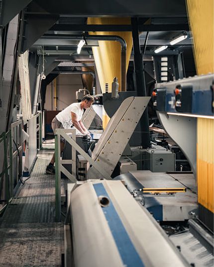 Medewerker aan het werk tussen industriële machines in een textielproductieomgeving.